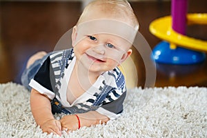 Portrait of cute adorable blond Caucasian smiling baby boy with blue eyes lying on floor in kids children room