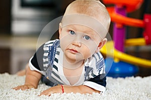 Portrait of cute adorable blond Caucasian smiling baby boy with blue eyes lying on floor in kids children room