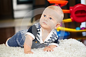 Portrait of cute adorable blond Caucasian smiling baby boy with blue eyes lying on floor in kids children room