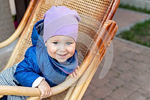 Portrait of cute adorable caucasian baby boy having fun sitting in  wooden rattan rocking chair on house terrace backyard outdoors