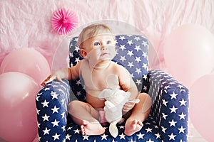 Portrait of cute adorable Caucasian baby girl with blue eyes sitting in blue children kids armchair with white stars celebrating