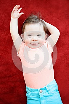 Portrait of cute adorable Caucasian smiling baby boy girl lying on floor red blanket in kids room