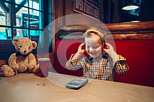 Portrait of cute adorable funny little boy toddler playing digital toy cell phone gadget with ear phones in a restaurant. Child