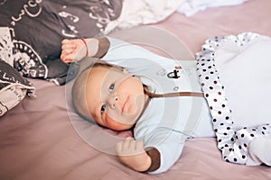 Portrait of cute adorable funny white Caucasian blond little baby boy newborn with blue grey eyes lying on large parents bed