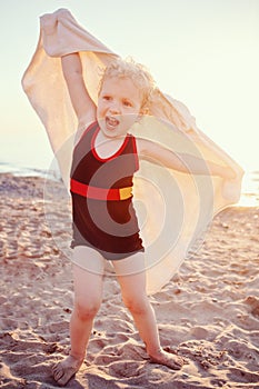 Portrait of cute adorable happy smiling toddler little girl with towel on beach making poses faces having fun