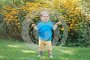 Portrait of cute adorable laughing smiling white Caucasian baby boy child standing among yellow flowers outside