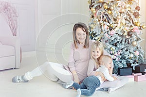 Portrait of cute adorable little blond children with mother enjoy sitting near christmas tree in cozy living room at home . Happy
