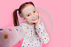 Portrait of cute adorable schoolgirl with tails dressed dotted shirt palm on cheekbone make selfie isolated on pink