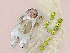 Portrait of a cute adorable smiling four month old baby boy lying on a bed with green apples