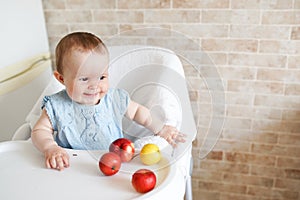 Portrait of cute adorable smiling laughing Caucasian child kid girl sitting in high chair eating apple fruit
