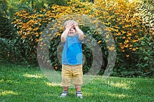 Portrait of cute adorable white Caucasian baby boy child standing among yellow flowers outside in garden park