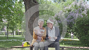 Portrait cute adult couple looking old photos remembering happy moments sitting on a bench in the park. Mature couple in