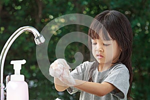 Portrait cute Asian girl aged 4 to 8 years old, washing her hands with soap from the tap. To clean her hands Frequent hand washing