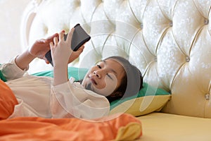 Portrait of cute asian girl on bed while use smartphone with attractive smiling at home