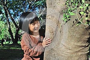 Portrait of a cute asian little girl hugging big tree.