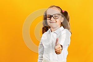 Portrait of a cute attractive little girl. The child shows thumb up on a yellow background