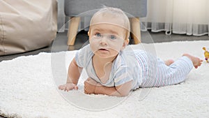 Portrait of cute baby boy with blue eyes lying on soft carpet in house