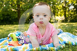 Portrait of Cute baby boy with Down syndrome lying on blanket in summer day on nature