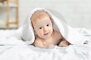 Adorable smiling baby boy lying on bed under white blanket