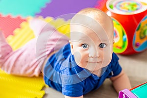 Portrait of cute baby boy lying on floor covered with multicolored soft mats in playroom. Adorable toddler kid smiling and playing