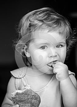 Portrait of cute baby with bread in her hands eating. Cute toddler child eating sandwich, self feeding concept.