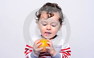 Portrait of a cute baby craving an orange.