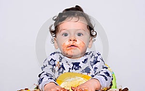 Portrait of a cute baby eating cake making a mess. Baby acting surprised trying to hide his mess.