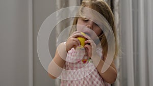 Portrait of cute baby girl in dress who eats a sour lemon while sitting indoors on high chair