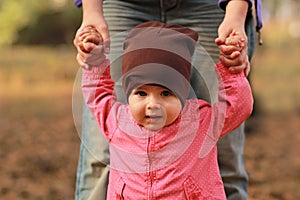 Portrait of a cute baby girl holding mom`s hands and learning to walk