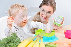 Portrait of a cute baby sitting on high chair while eating solid food