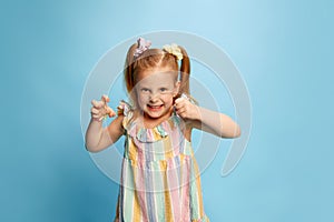 Portrait of cute, beautiful, redhead little girl, child standing with funny angry face against blue studio background.