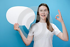 Portrait of cute beautiful young happy woman holding speech bubble posing isolated over blue background wall