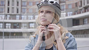 Portrait cute blond woman putting a bike helmet on her head and riding her bicycle against the background of urban