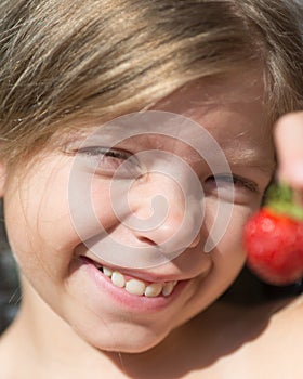 Portrait of cute blonde Caucasian girl is holding a red berry in her hand. Girl is smiling