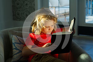 Portrait of cute blonde child reading interesting kids book story. Child reading book at home. Little boy sitting on
