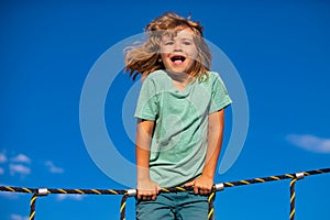 Portrait of cute boy child doing rock climbing and monkey bars in the playbackground. Funny kids face.