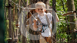 Portrait of cute boy holding safety rope at outdoor extreme adventure park. Active childhood, healthy lifestyle, kids playing