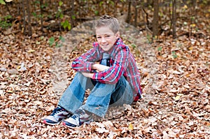 Portrait of cute boy sitting in leaves with legs crossed.