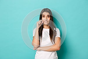 Portrait of cute brunette woman in white t-shirt making promise, seal lips, zipping mouth to hide secret, standing over