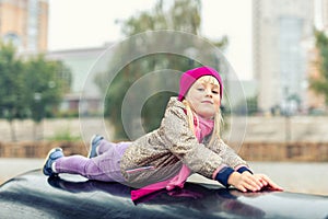 Portrait of cute caucasian blond little girl having fun playing at modern outdoor playground at city park in autumn