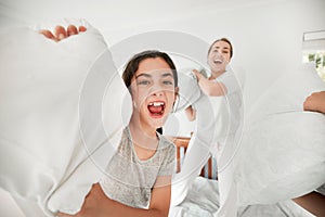 Portrait of cute caucasian daughter and mother having a fun pillow fight at home. Happy young girl and mother holding