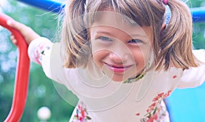 Portrait of cute Caucasian litte girl wearing white dress with flowers hanging on monkey bars on a summer day. Girl