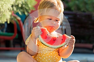 Portrait of cute Caucasian little girl with dirty mouth in yellow swimwear funny eating a slice of fresh watermelon