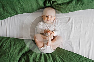 Portrait of a cute charming smiling laughing Caucasian white boy of six months old lying on a bed and looking at the camera