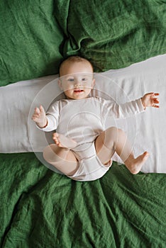 Portrait of a cute charming smiling laughing Caucasian white boy of six months old lying on a bed and looking at the camera. View