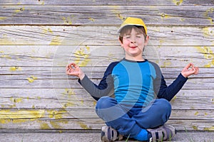 Portrait of a cute cheerful boy with yellow cap sitting outdoors in yoga pose