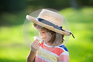 Portrait of a cute child boy in straw hat smelling plumeria flower. Close up caucasian kids face. Closeup head of funny