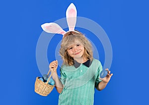 Portrait of cute child with bunny ears hold easter basket with easter eggs, isolated on studio background.