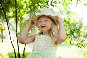 Portrait of cute child girl model in hat smiling in park or outdoor. Happy childhood, summer holidays and vacations