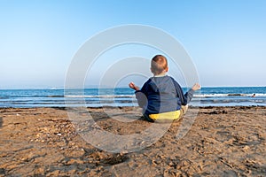Portrait of a cute child sitting on a rocks near the sea. Meditation wellness